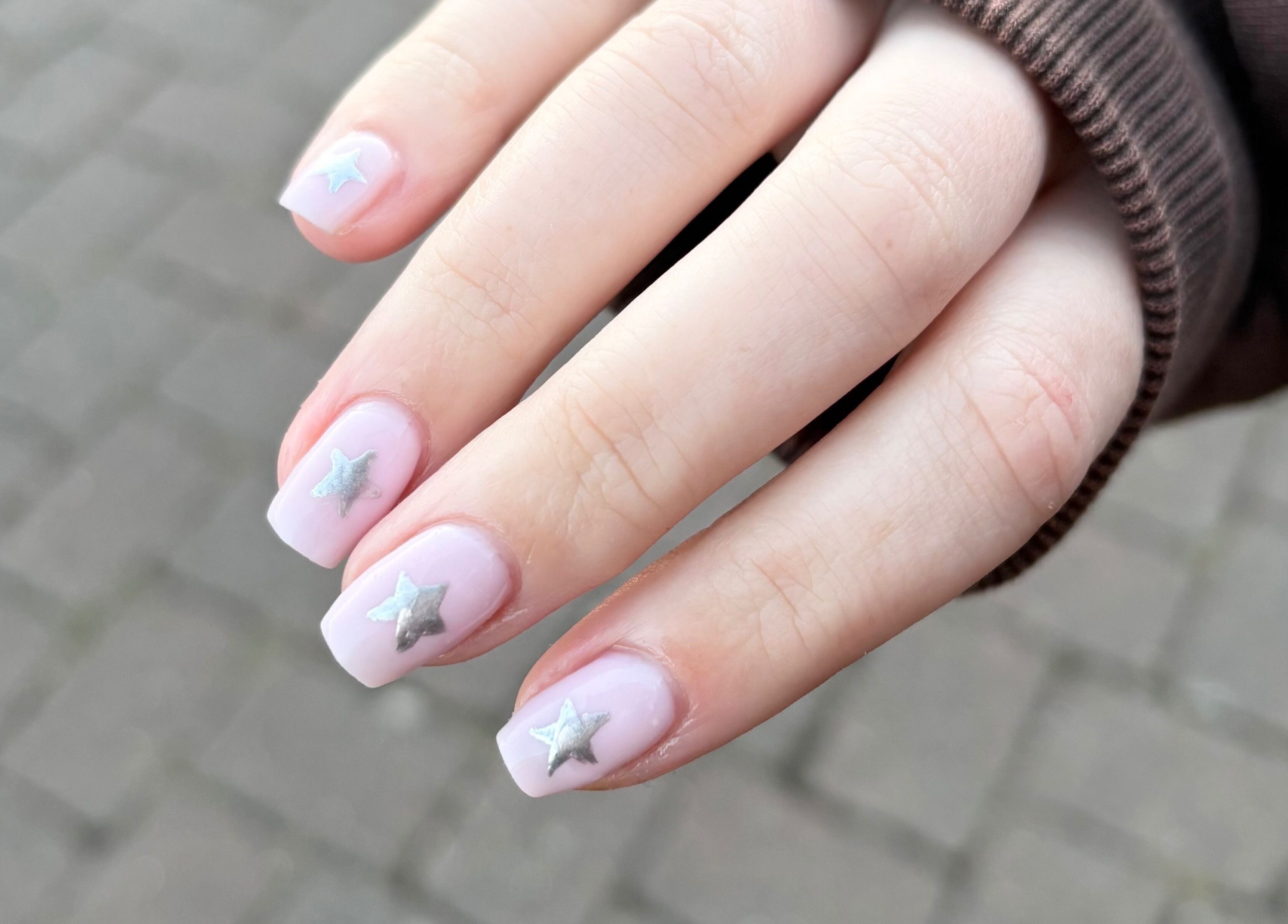 Close-up of a hand showing pink nails with silver stars at Glos Nails by April, Shirley, England, GB.