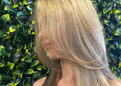 Blonde hair styled with volume at SBKHair&Beauty, Crestmead, Queensland, AU, against a leafy background.
