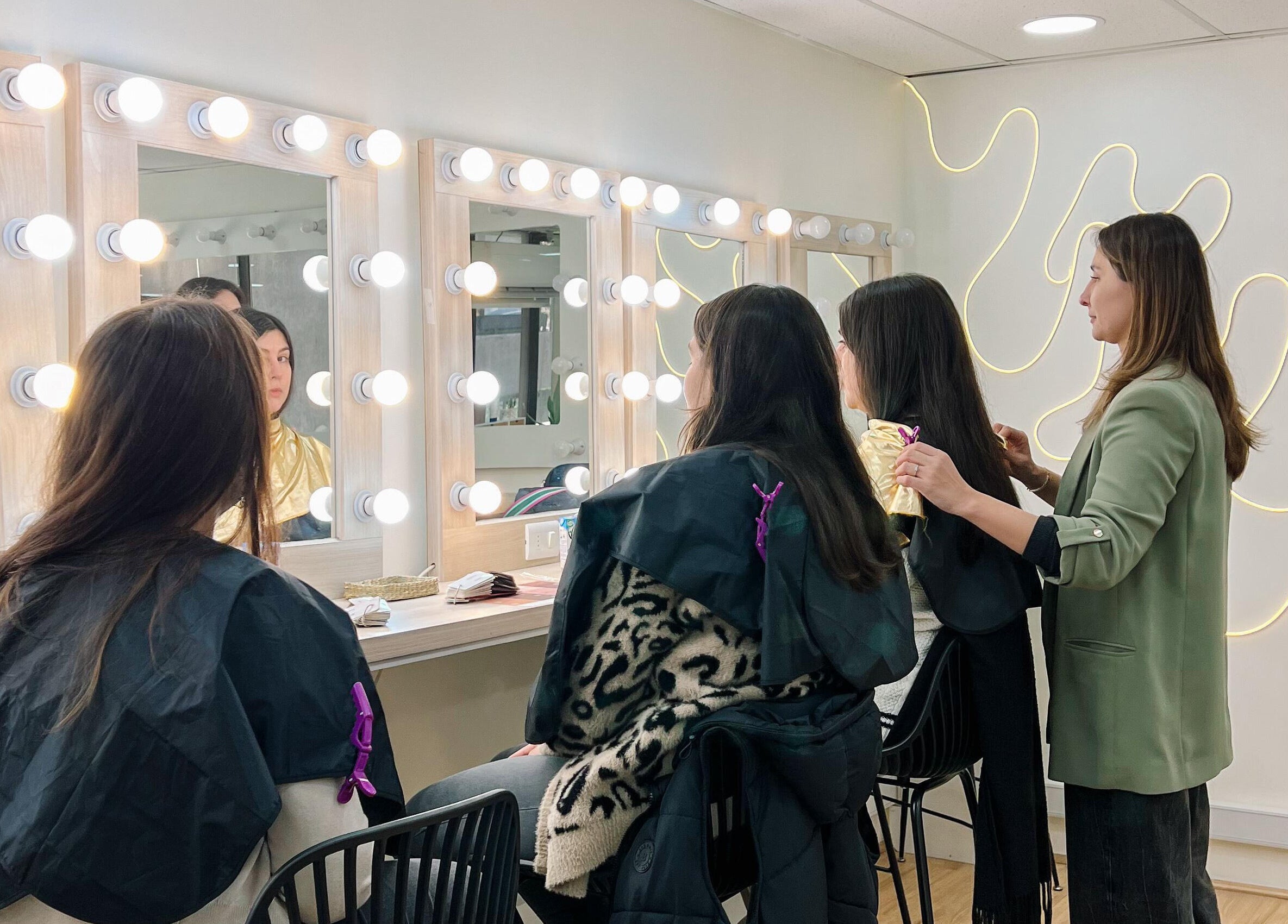 Estilista en The Beauty Room peinando a clienta en Las Condes, Región Metropolitana, CL con espejos iluminados.