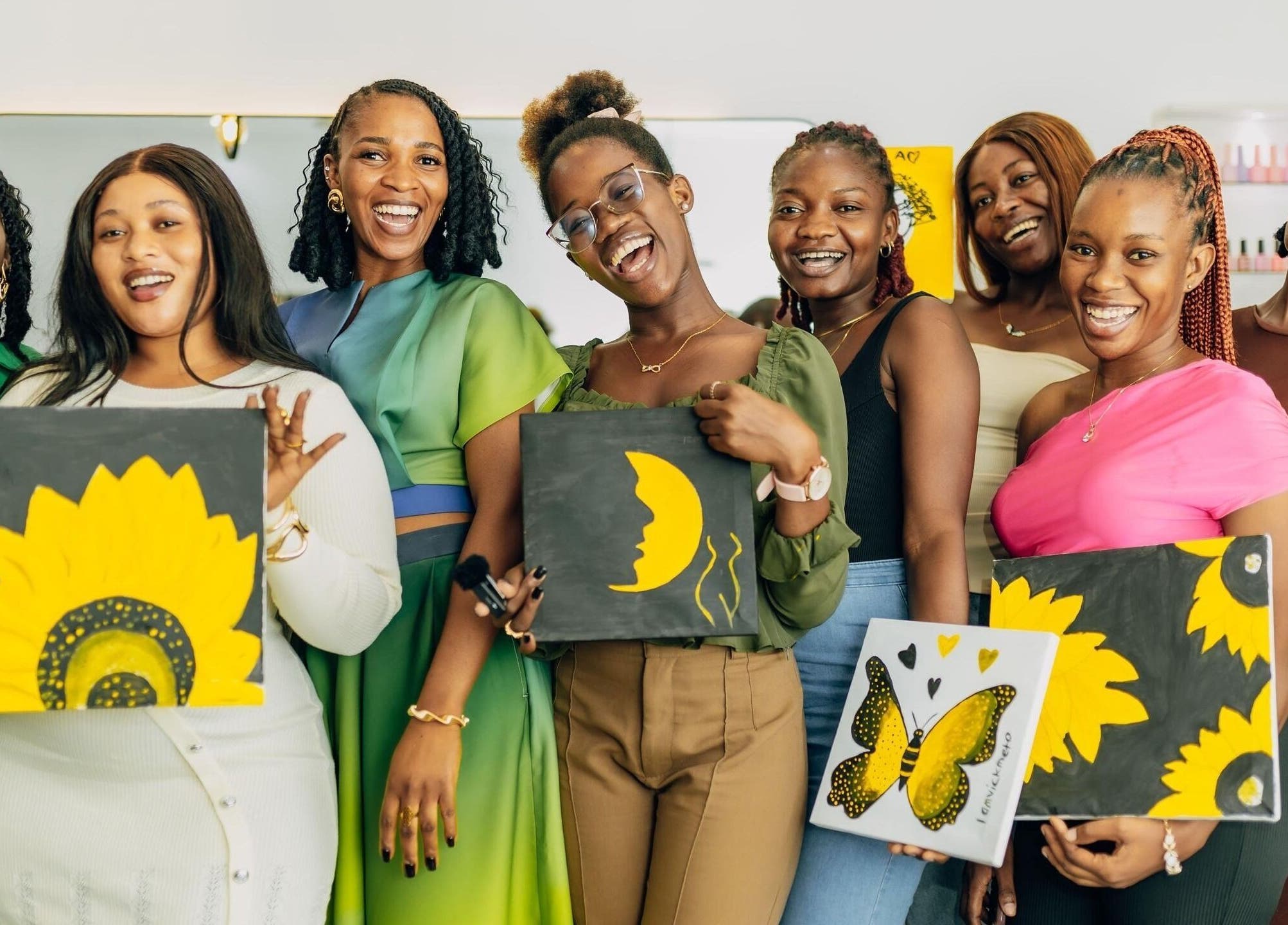 Women celebrate creativity at Ronexe Beauty Hub, Greater Accra Region, GH with painted canvases and smiles.