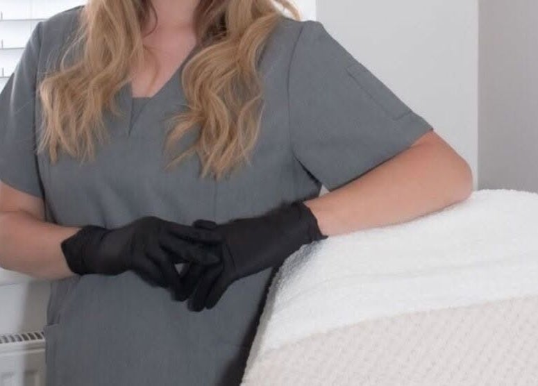 Beauty professional at Radiant Skin By KB in Rhyl, Wales, GB, wearing grey uniform and black gloves.