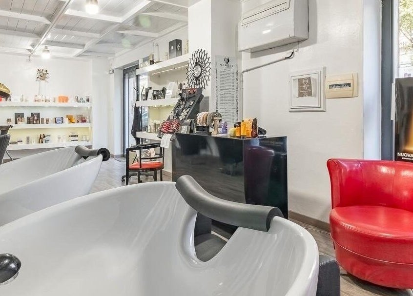 Interno elegante di Venere Parrucchieri ad Alghero, Sassari, IT con lavandini bianchi e poltrona rossa.