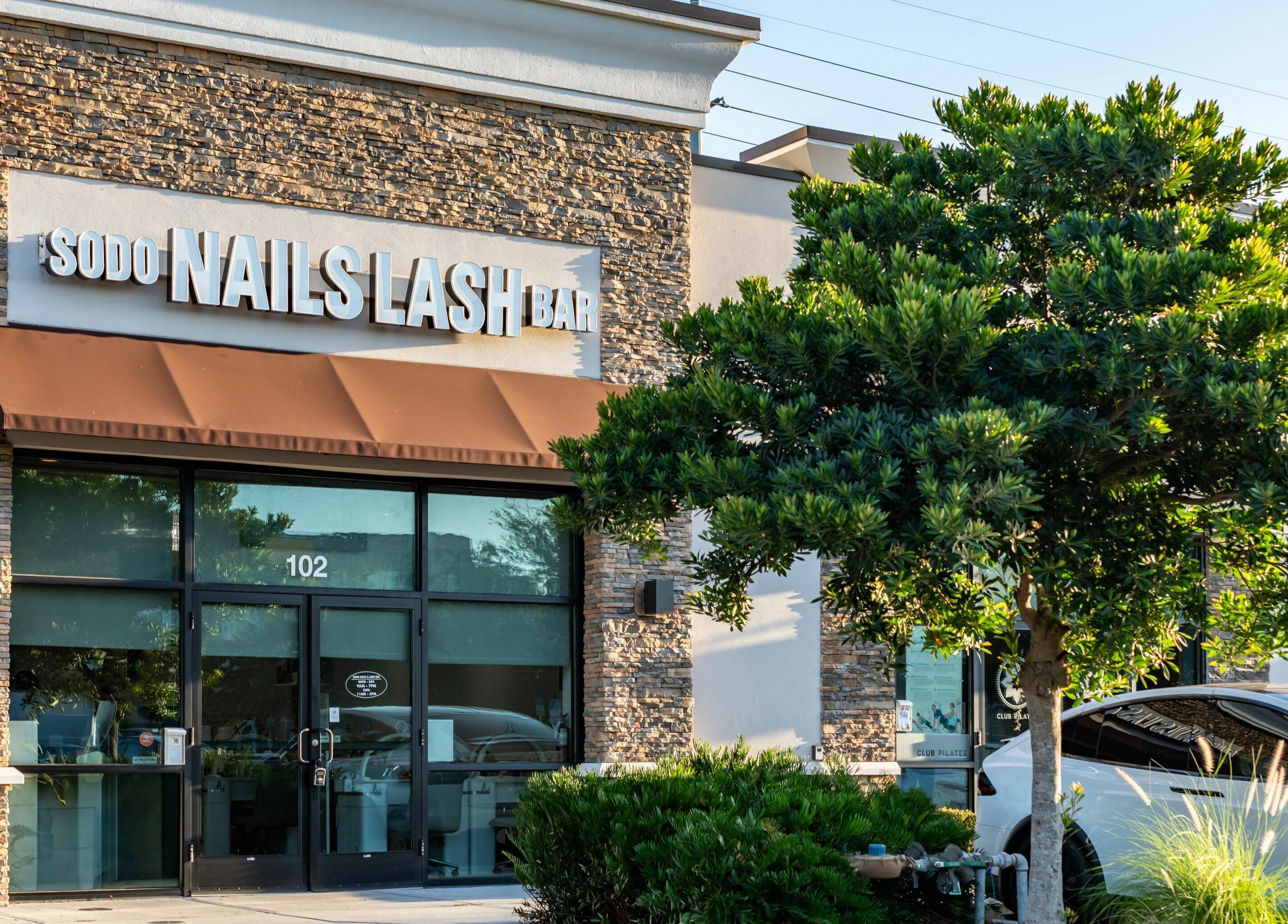 Exterior of SODO Nails & Lash Bar in Orlando, Florida, US with stylish storefront and lush greenery.