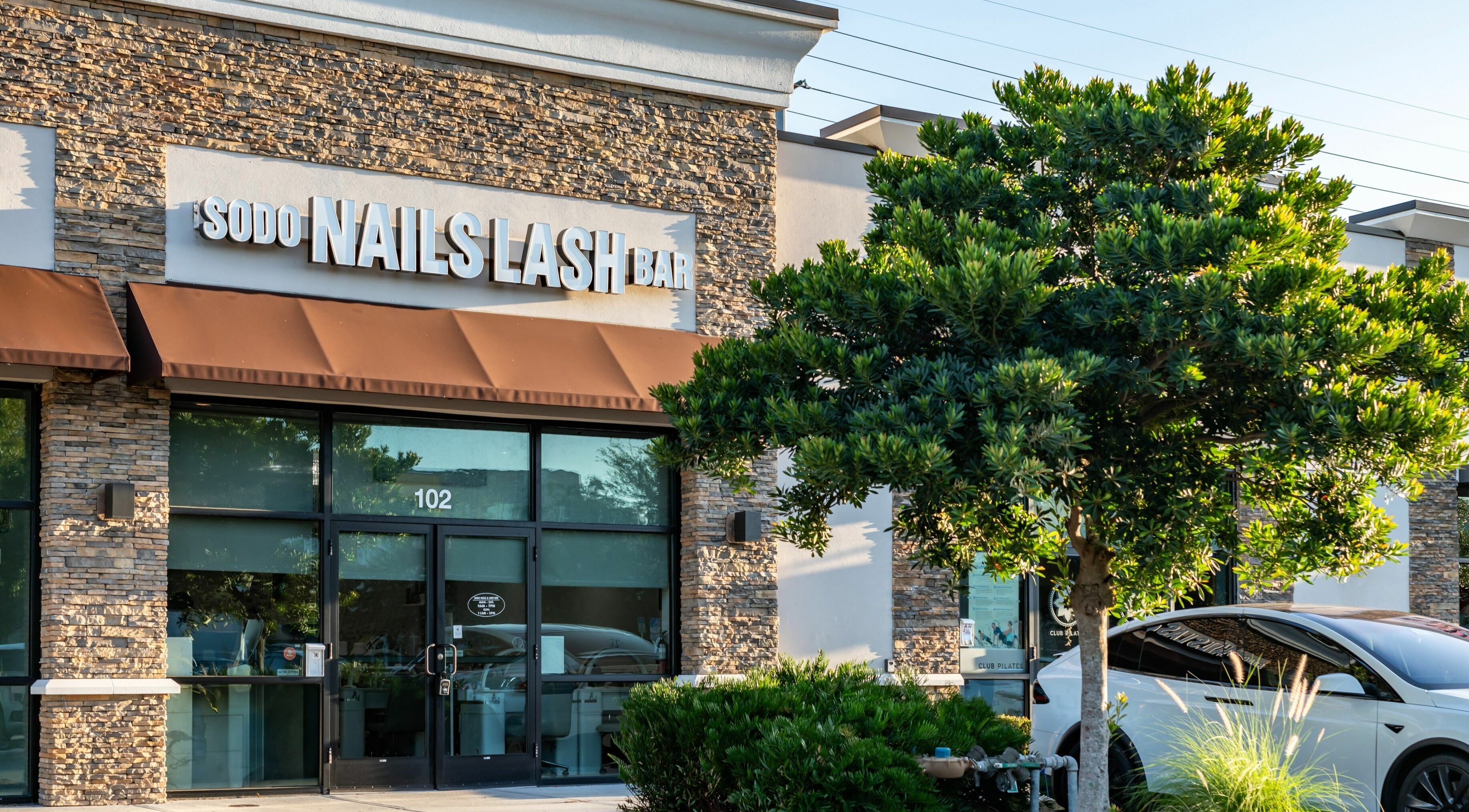 Exterior of SODO Nails & Lash Bar in Orlando, Florida, US with stylish storefront and lush greenery.