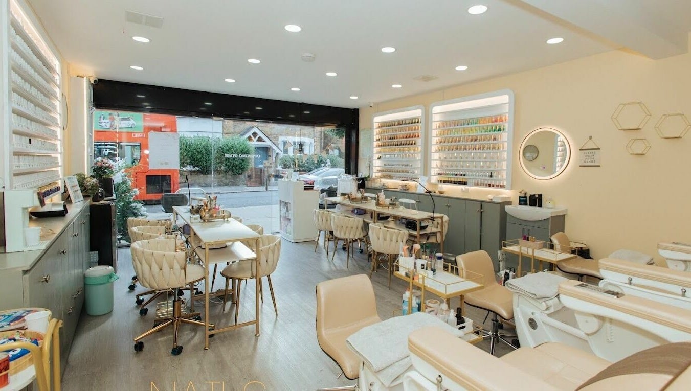 Lux Nail Spa & Beauty in London, England offers a chic, modern interior with plush seating and extensive nail polish display.