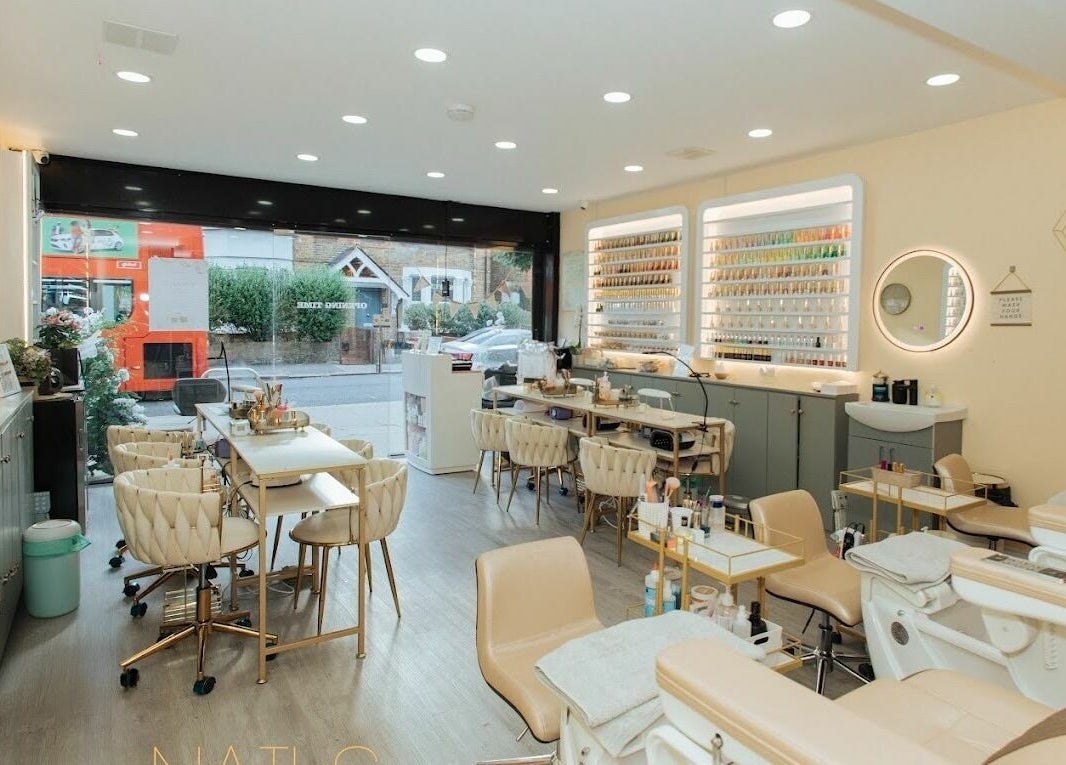 Lux Nail Spa & Beauty in London, England offers a chic, modern interior with plush seating and extensive nail polish display.