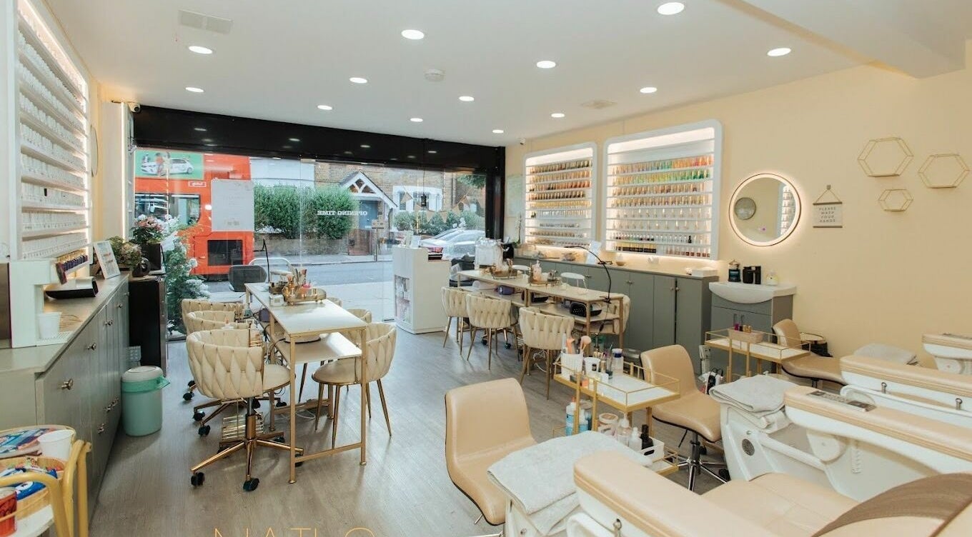 Lux Nail Spa & Beauty in London, England offers a chic, modern interior with plush seating and extensive nail polish display.