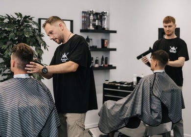 Professional barbers at MAD BARBERS in Jelgava, LV, styling clients' hair in a modern salon setting.