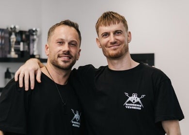 Two barbers at MAD BARBERS in Jelgava, LV smiling in a welcoming barber shop setting.