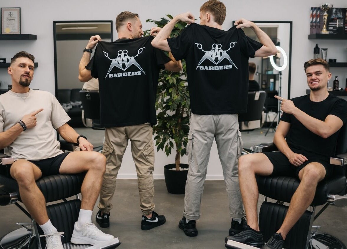 MAD BARBERS team in Jelgava showcasing branded t-shirts in a stylish barbershop setting.