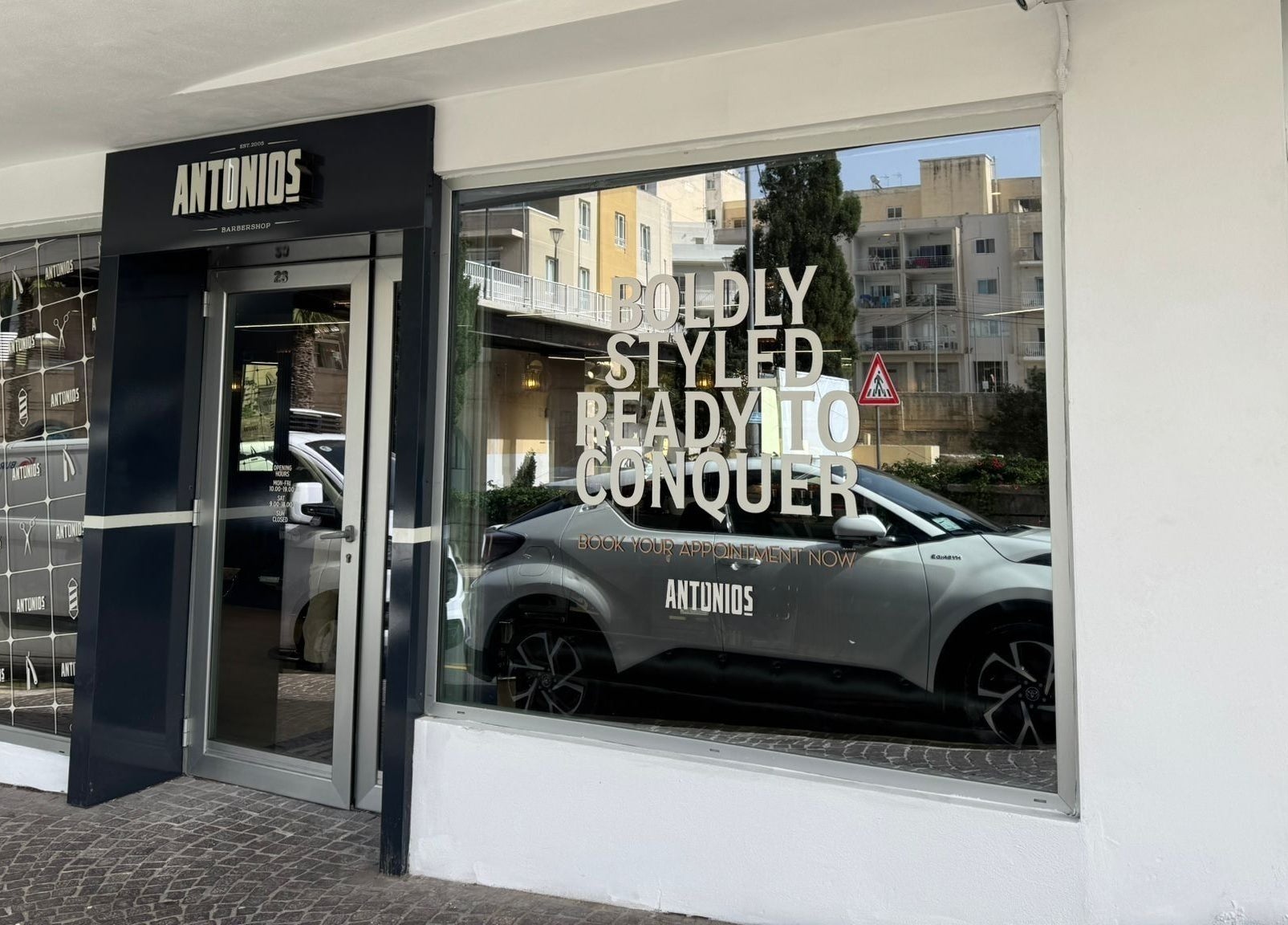 Front entrance of Antonio's Barbershop Spinola Park at San Ġiljan, MT with bold lettering on the window.