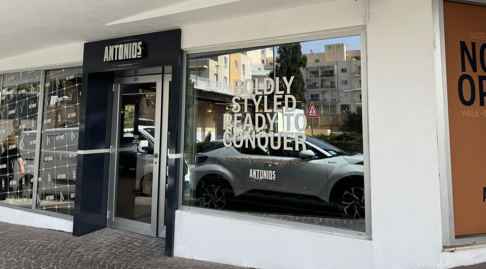 Front entrance of Antonio's Barbershop Spinola Park at San Ġiljan, MT with bold lettering on the window.