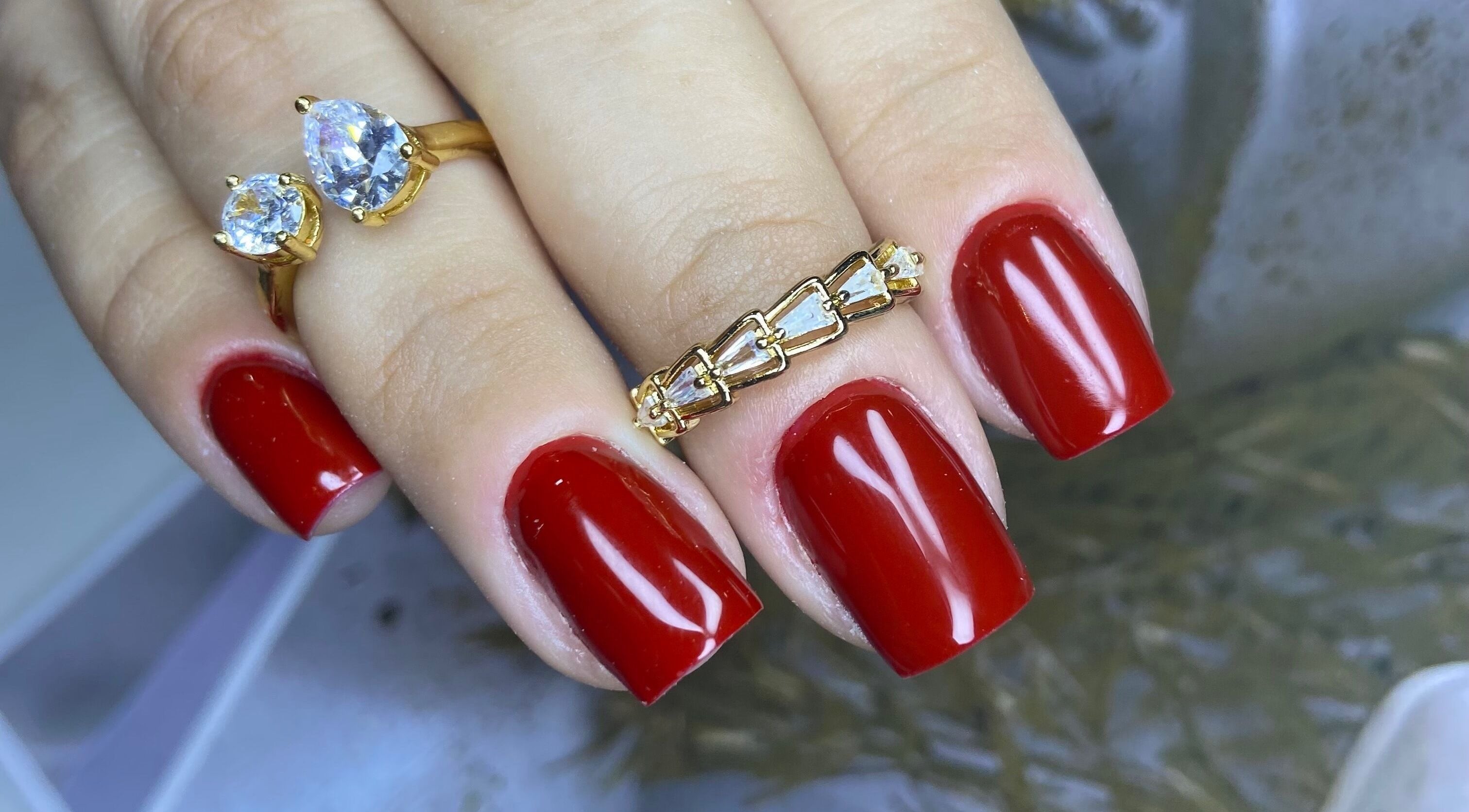 Unhas vermelhas elegantes com anéis de luxo no Studio Carol Florez, São Paulo.