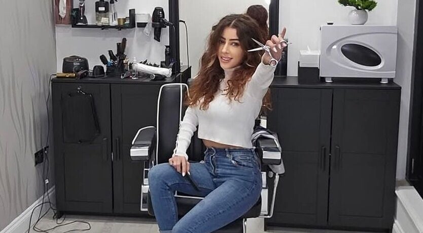 Hair stylist at Sabi Style salon, Edgware, England, GB, holding scissors in chic salon setting.