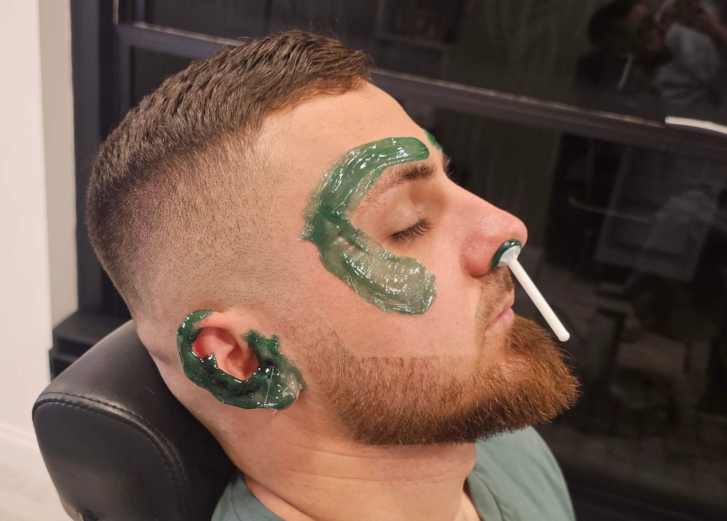 Man receiving facial waxing at Sabi Style, Edgware, England, GB. Green wax applied to eyebrows and face.