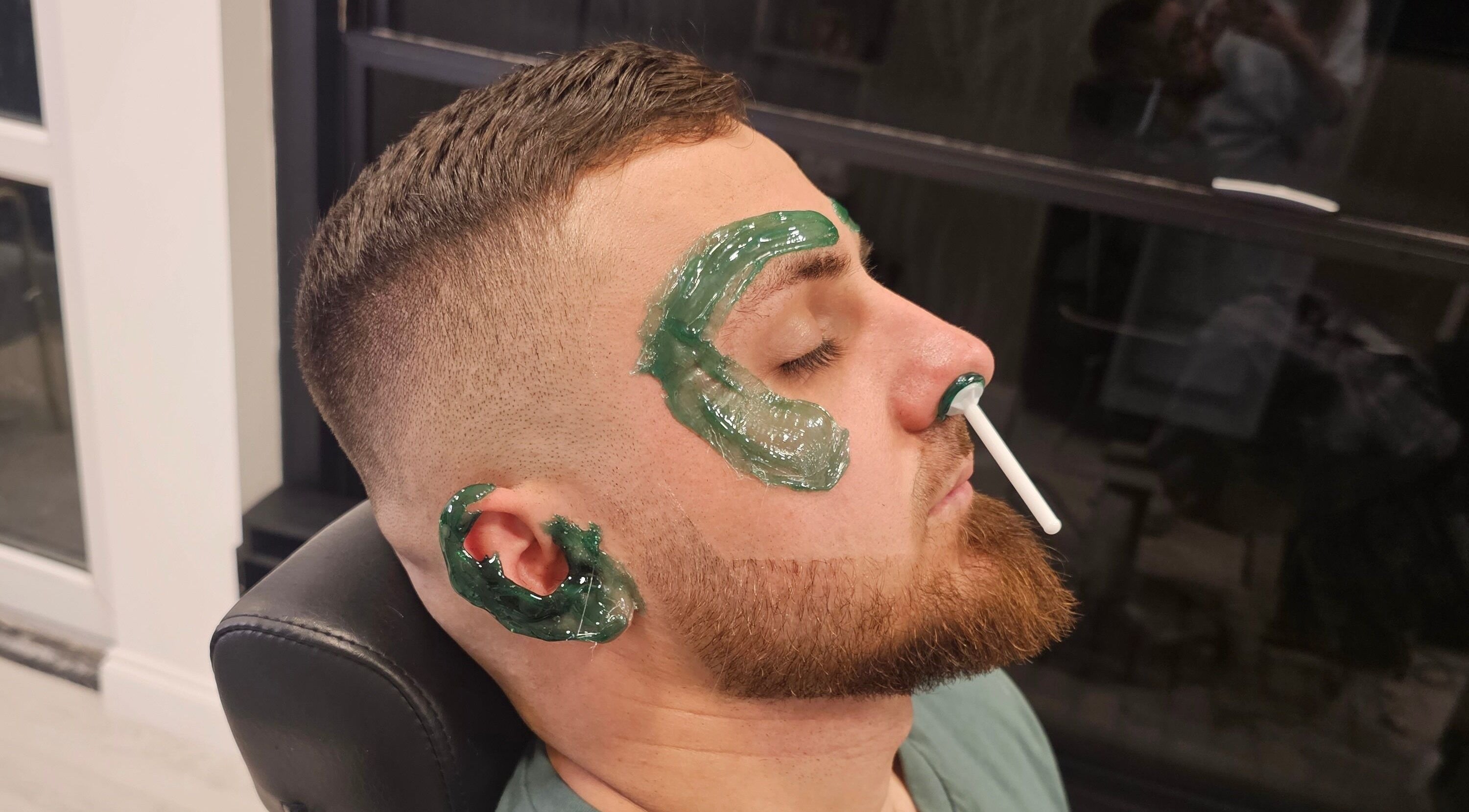 Man receiving facial waxing at Sabi Style, Edgware, England, GB. Green wax applied to eyebrows and face.