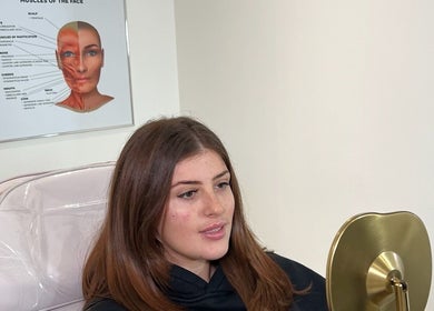 Client at AESTHETICS. By Nurse Ryan, Glasgow smiling while holding a mirror during a consultation.