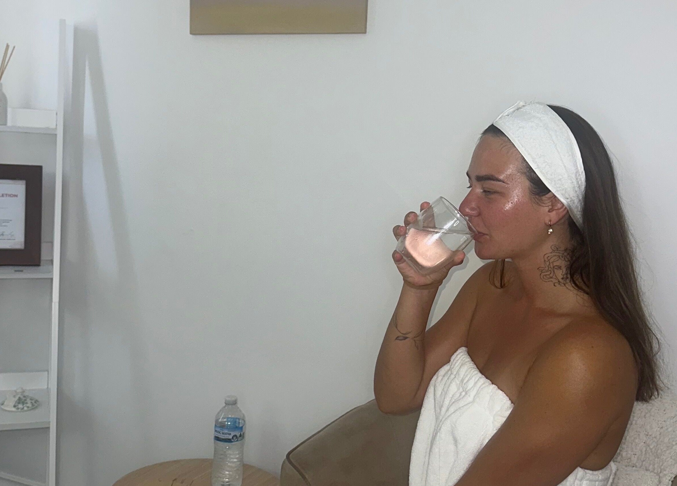 Client enjoying a relaxing moment at Glowy With B, Melbourne, Victoria, AU, sipping water in a cozy spa setting.