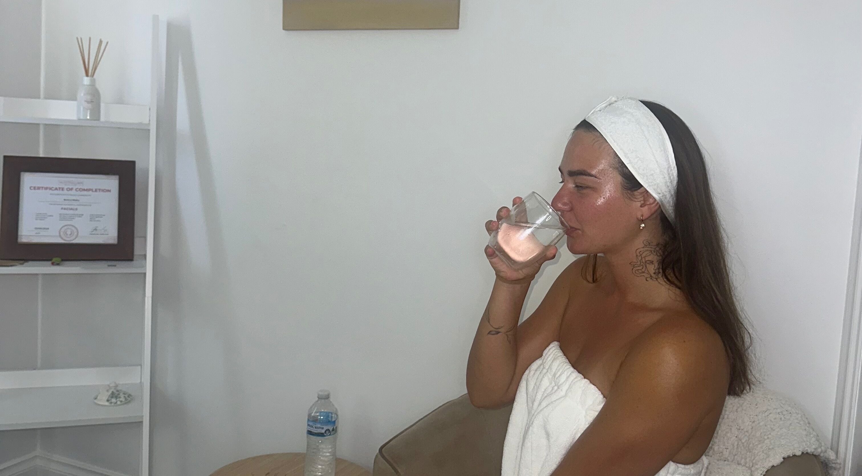 Client enjoying a relaxing moment at Glowy With B, Melbourne, Victoria, AU, sipping water in a cozy spa setting.