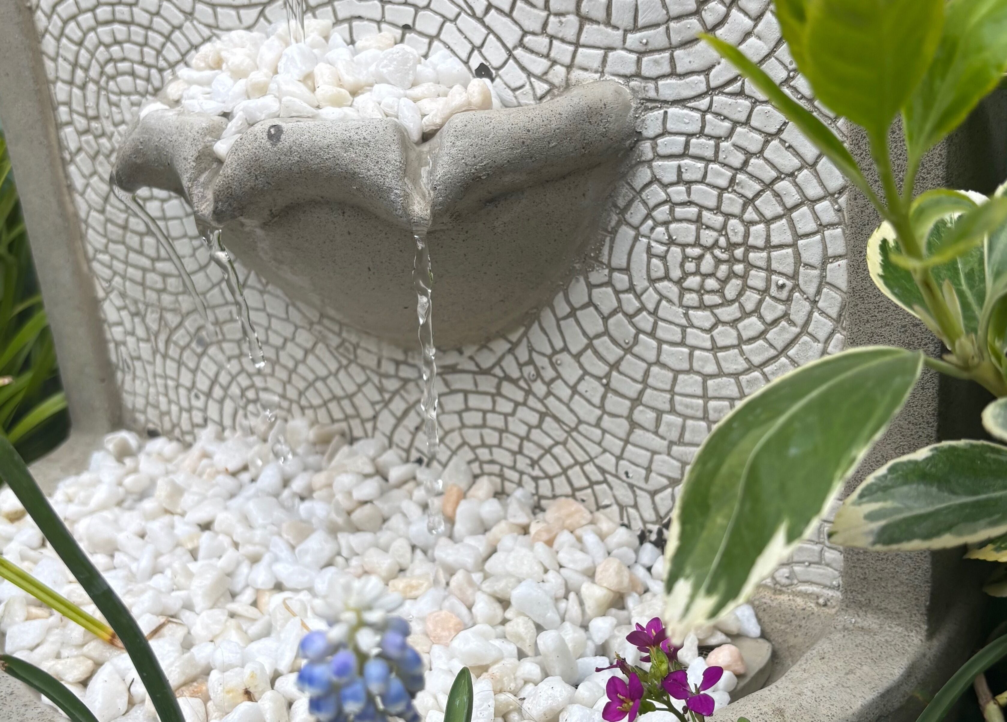 Stone fountain at Rhilax, Ilkeston, England, GB with cascading water and lush greenery.