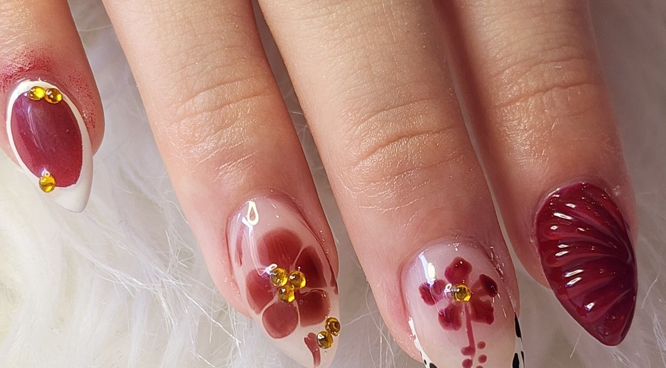 Elegant floral nail art by Kay at Flora's Salon & Spa, Flora, Indiana, US. Detailed red designs with rhinestones.