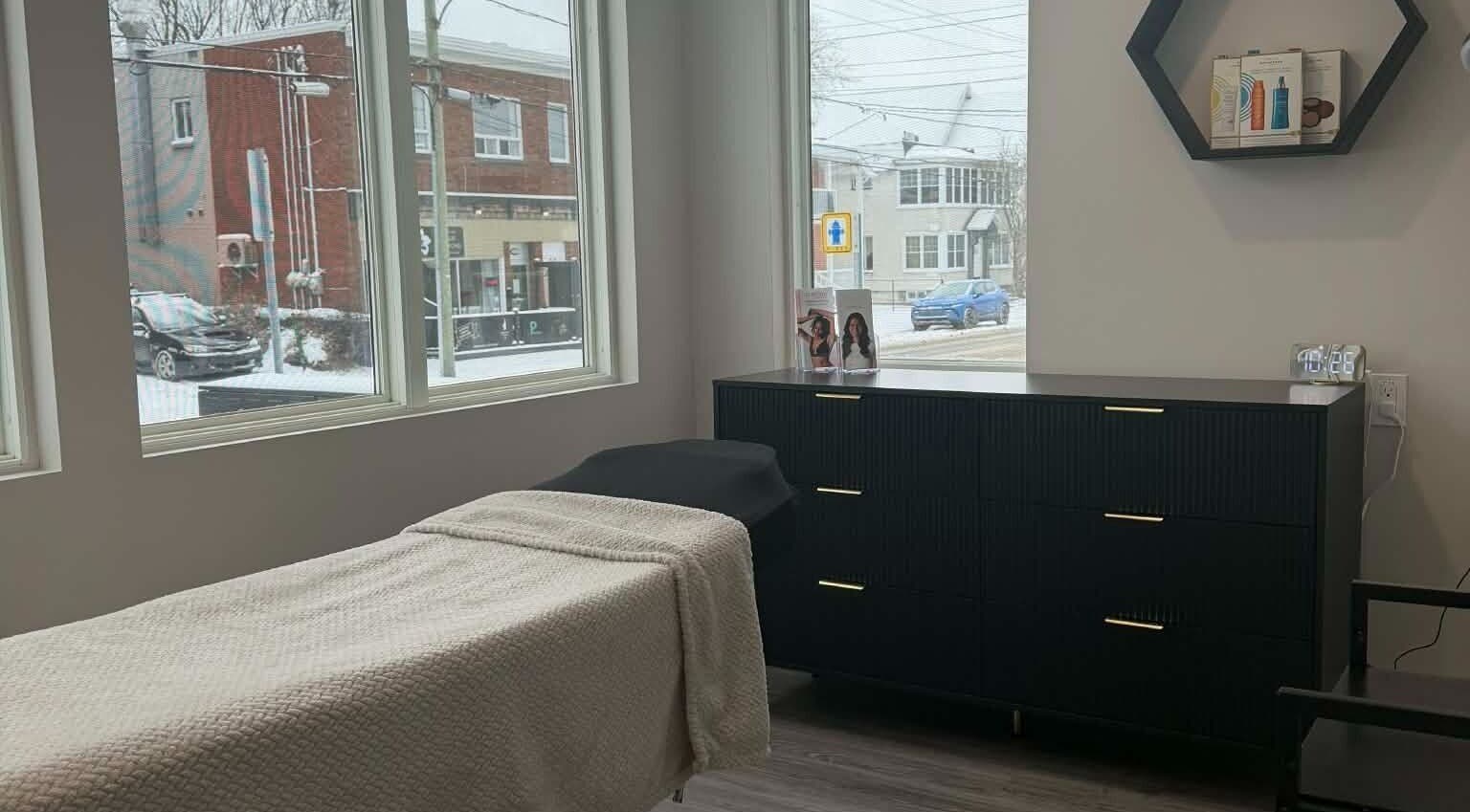 Salle de soin lumineuse chez Naturel Skin, Granby, Québec, CA, avec table confortable et vue extérieure.
