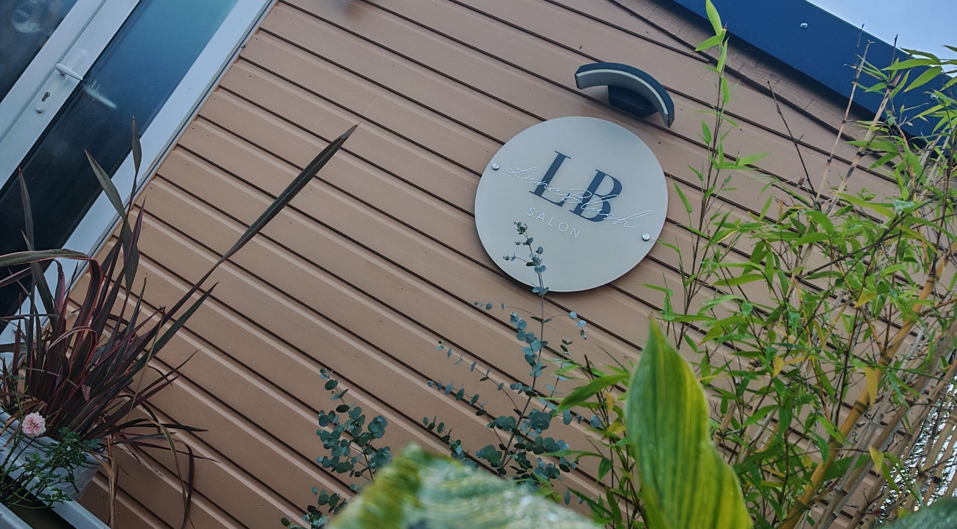 Exterior view of Luna Blush salon in Highworth, England, GB with branded sign and lush plants.