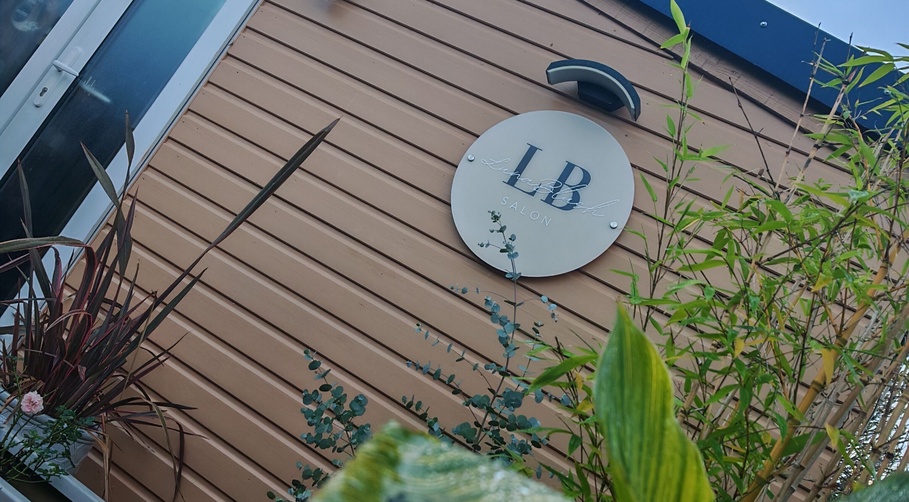Exterior view of Luna Blush salon in Highworth, England, GB with branded sign and lush plants.