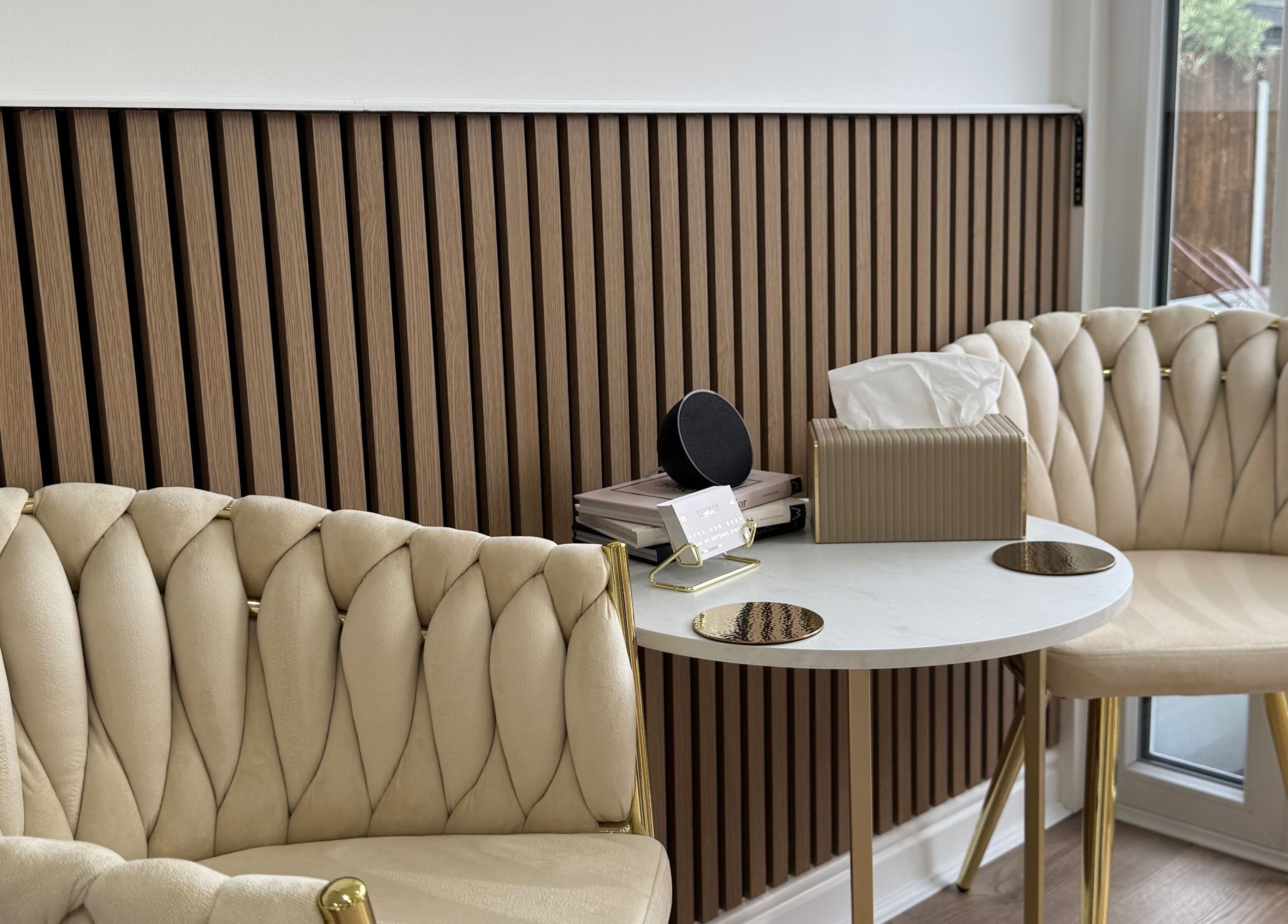 Elegant seating area at Defined Studio in Bowers Gifford, England. Plush chairs with a modern table and wood panel backdrop.