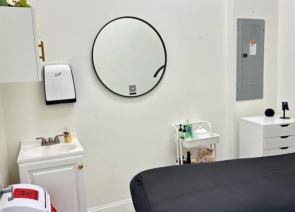 Sala de tratamiento en Daylook: The Beauty in Your Hands, Miami, Florida, US, con espejo redondo y cama negra.