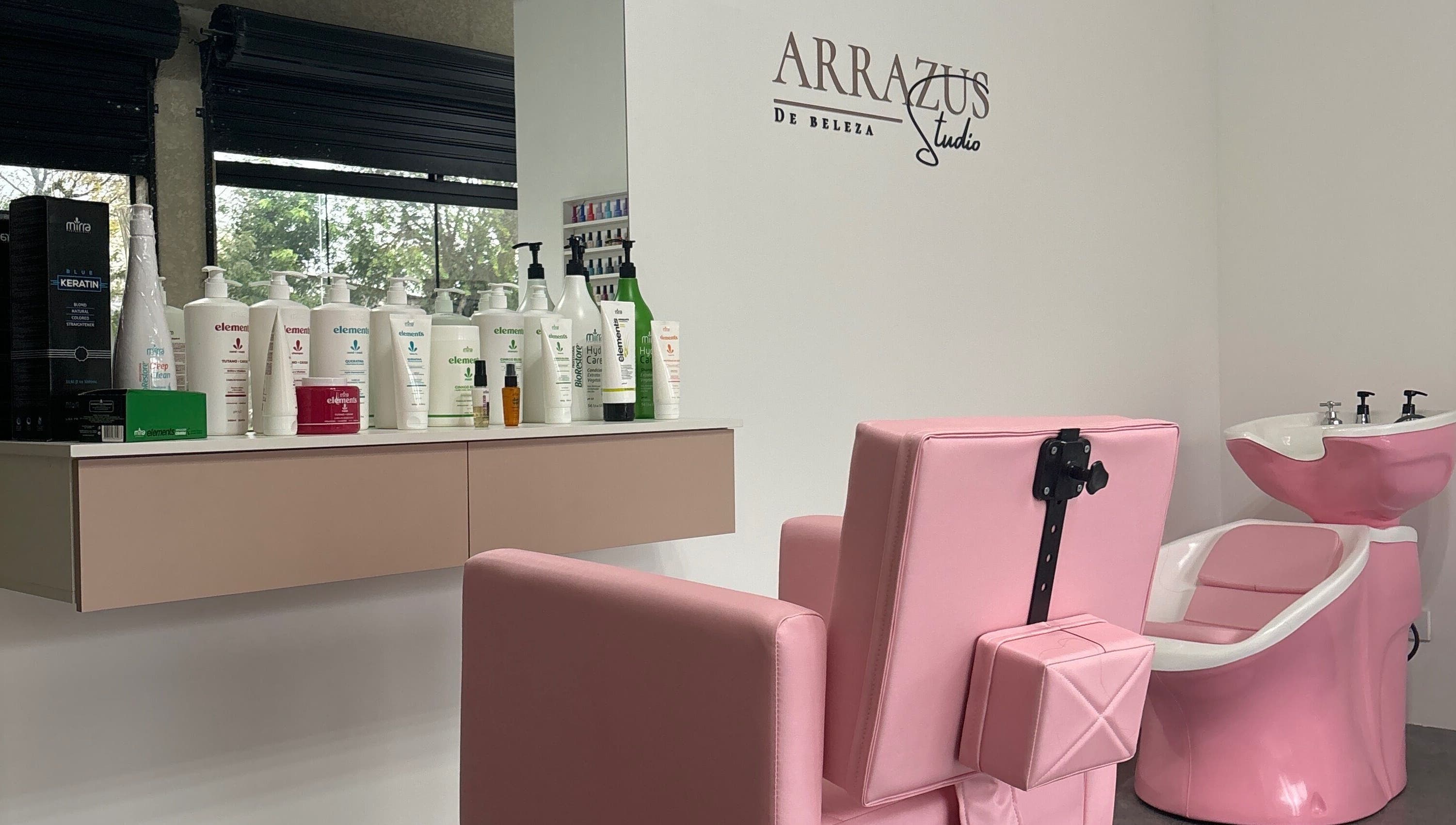 Interior do Arrazus Studio de Beleza com cadeira rosa e produtos na bancada, Paraná, Paraná, BR.