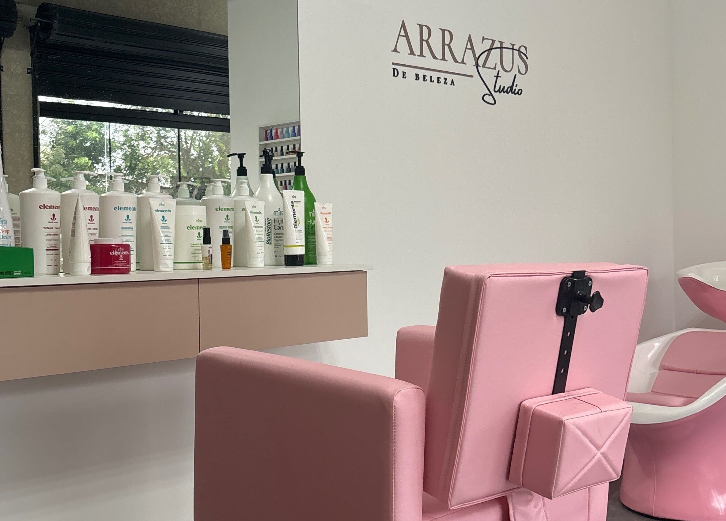 Interior do Arrazus Studio de Beleza com cadeira rosa e produtos na bancada, Paraná, Paraná, BR.