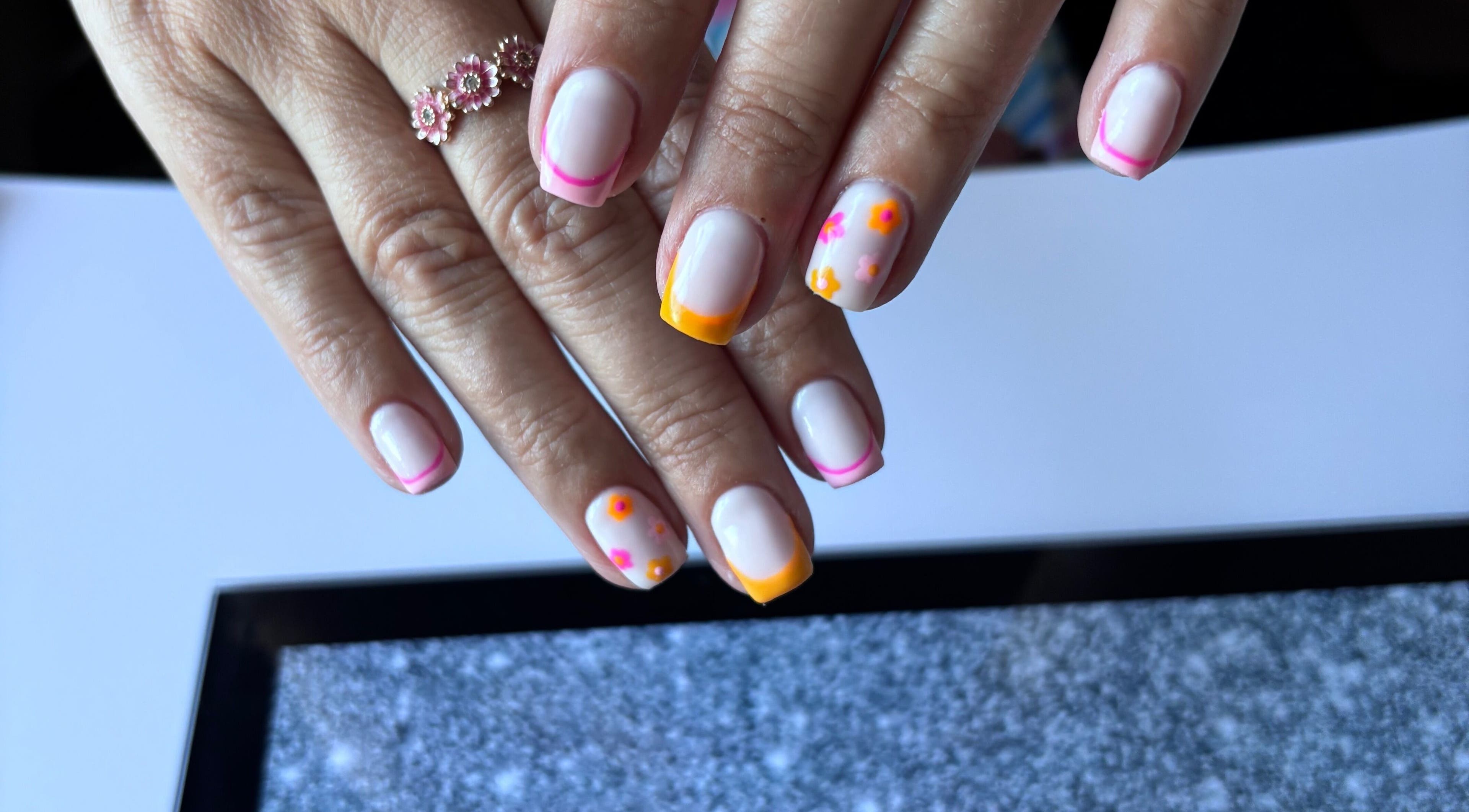 Colorful floral nail art at Freyas Beauty, Bream, England, GB, showcasing vibrant pink and orange designs.