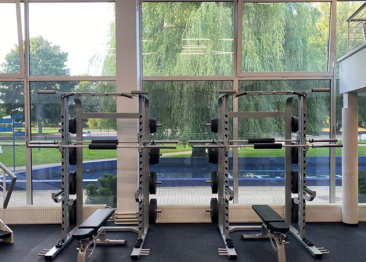 Modern gym with weight machines at Vantis Sporta un veselības centrs, Rīga, LV, overlooking lush greenery.