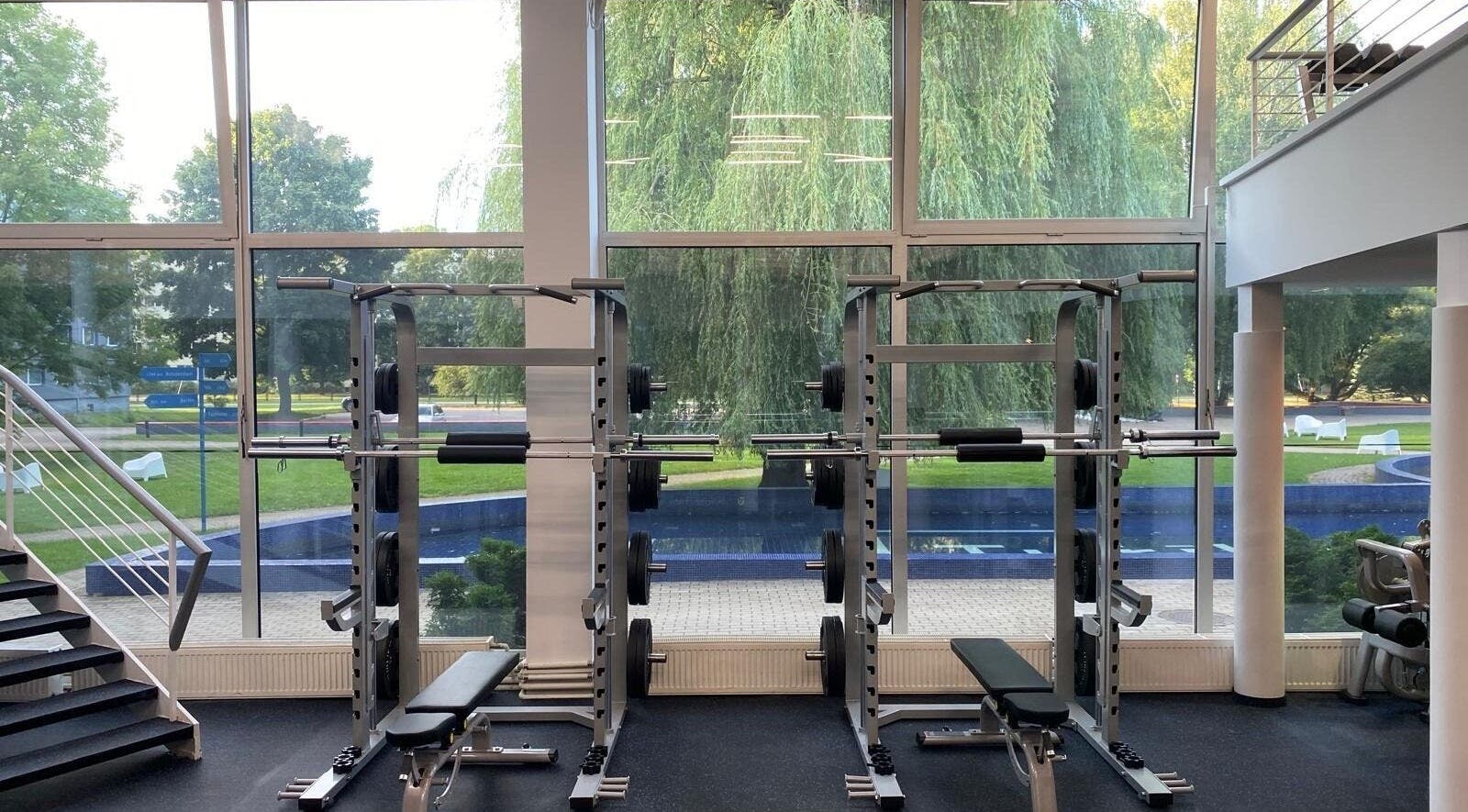 Modern gym with weight machines at Vantis Sporta un veselības centrs, Rīga, LV, overlooking lush greenery.