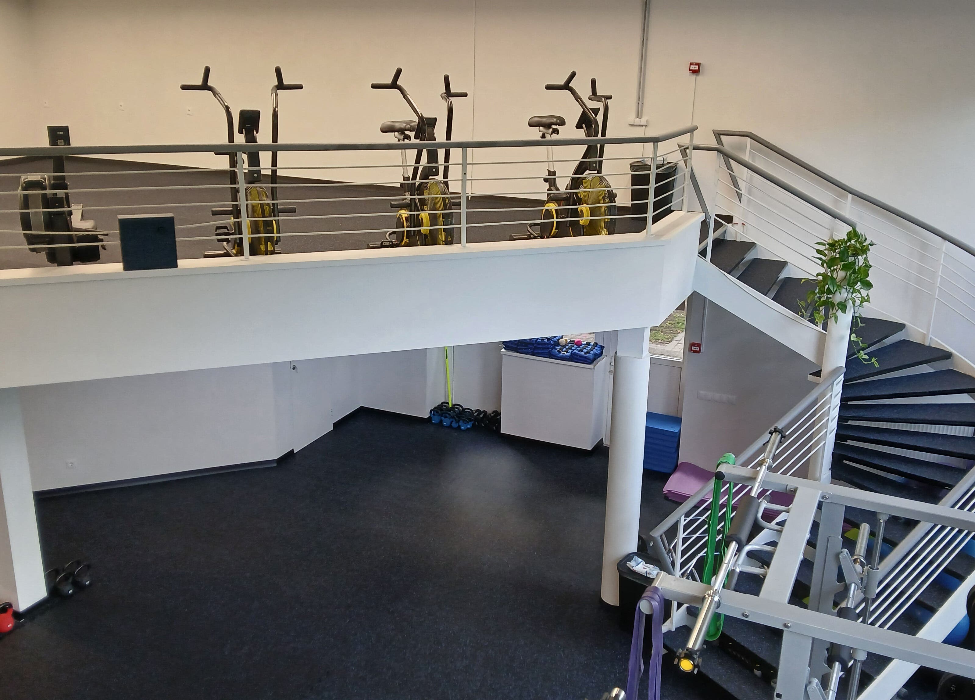 Bright gym space at Vantis Sporta un veselības centrs, Rīga, LV with modern exercise equipment and a spiral staircase.