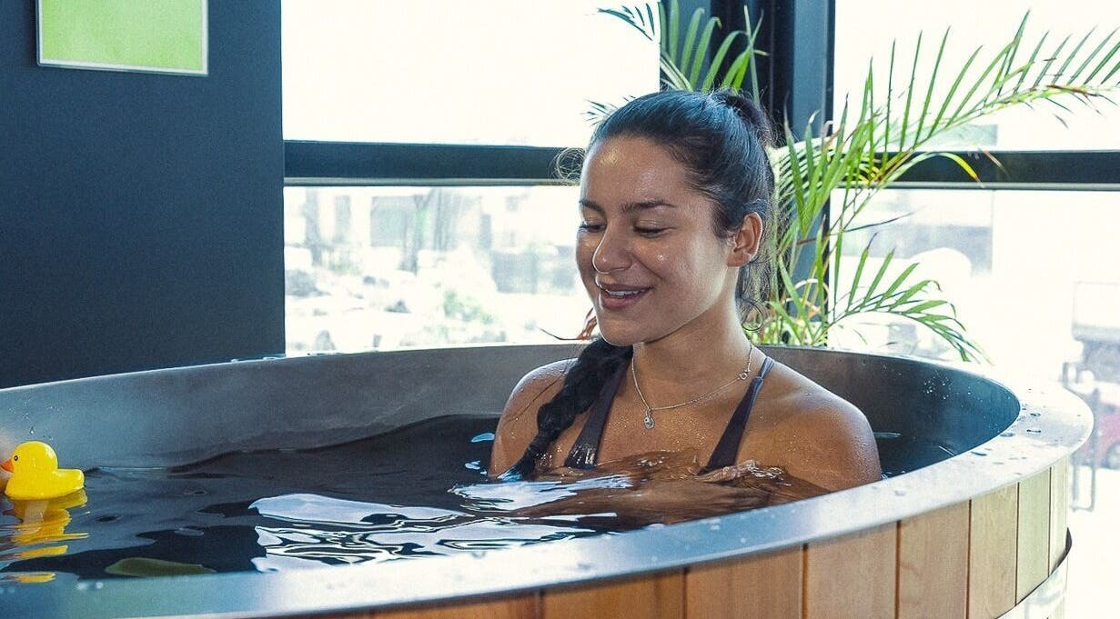 Woman relaxing in a tub at Energize Recovery, Melbourne, Victoria, AU, with a rubber ducky and lush plants.