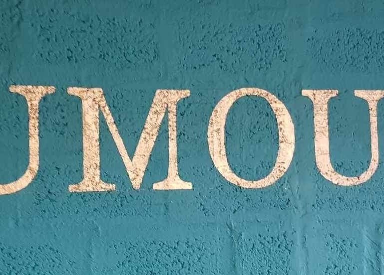 Weathered 'Rumours' text on a textured blue wall at Rumours, Brodick, Scotland, GB.