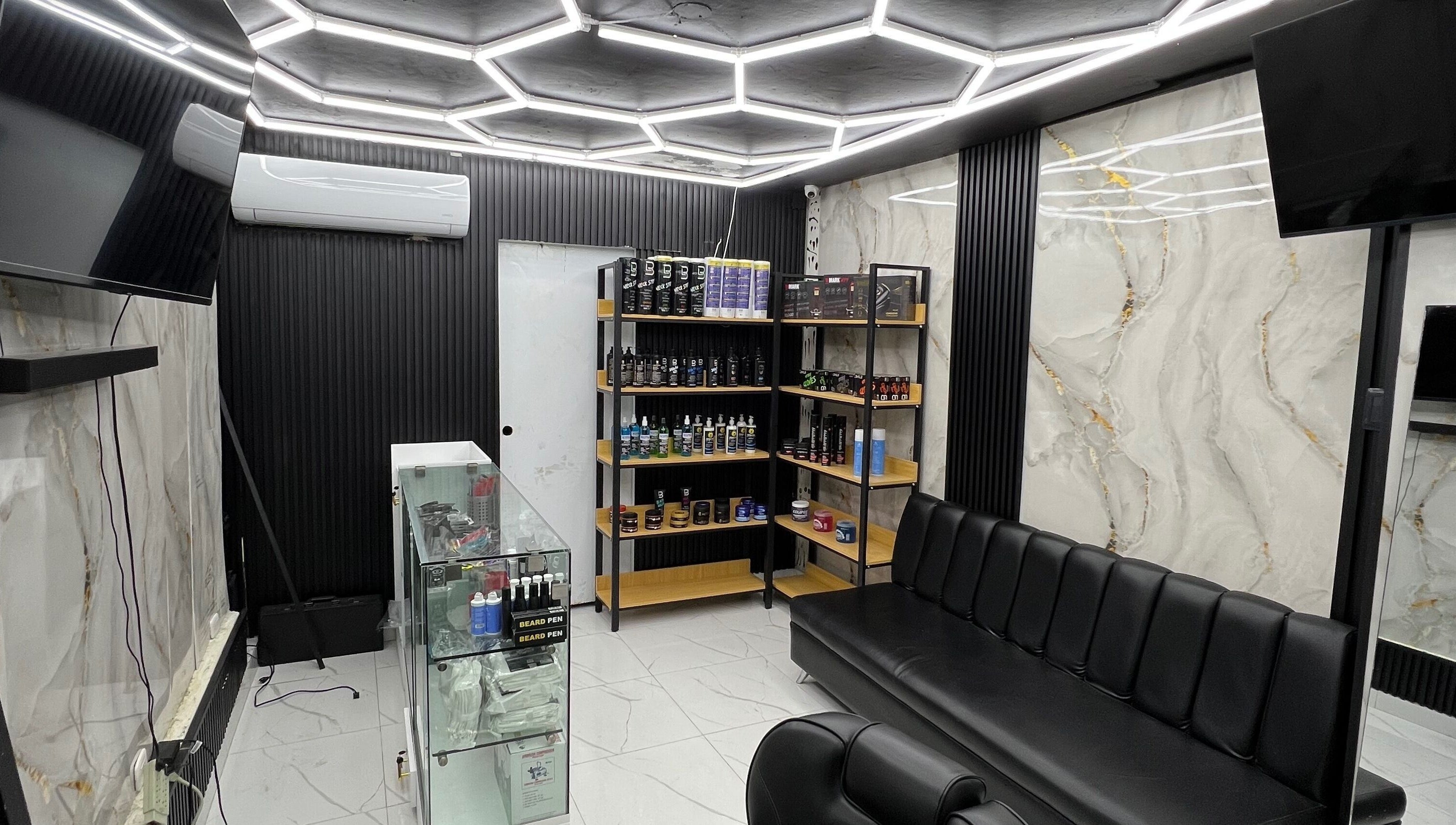 Interior moderno de GECS BARBER STUDIO en Santo Domingo, DO, con estantería y asientos elegantes.