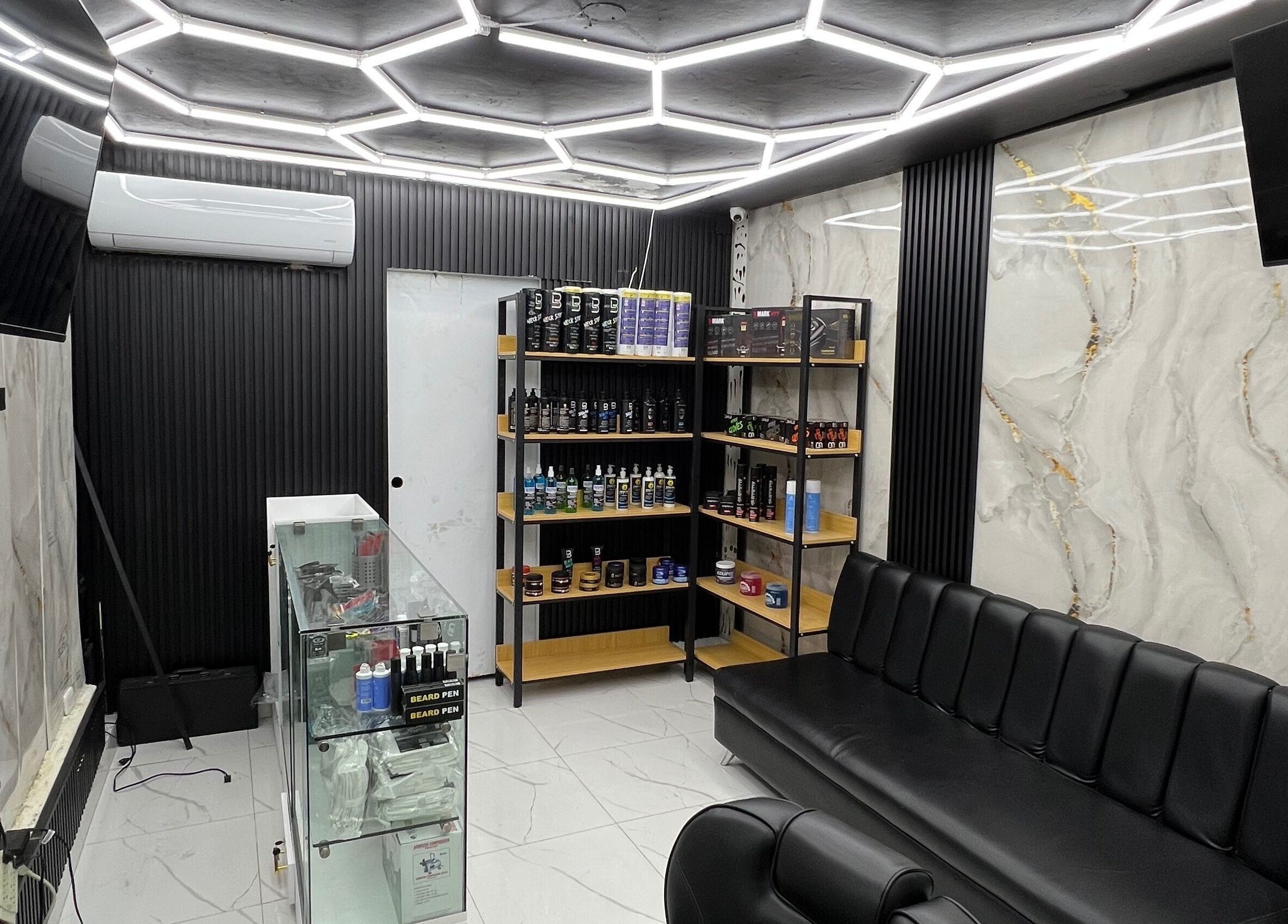 Interior moderno de GECS BARBER STUDIO en Santo Domingo, DO, con estantería y asientos elegantes.