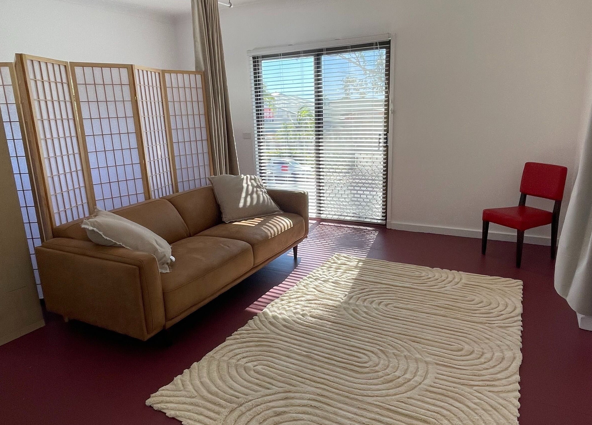 Cozy lounge area at The Biofield Body - Byron Bay, featuring a comfy sofa, red chair, and soft lighting in Byron Bay, New South Wales, AU.