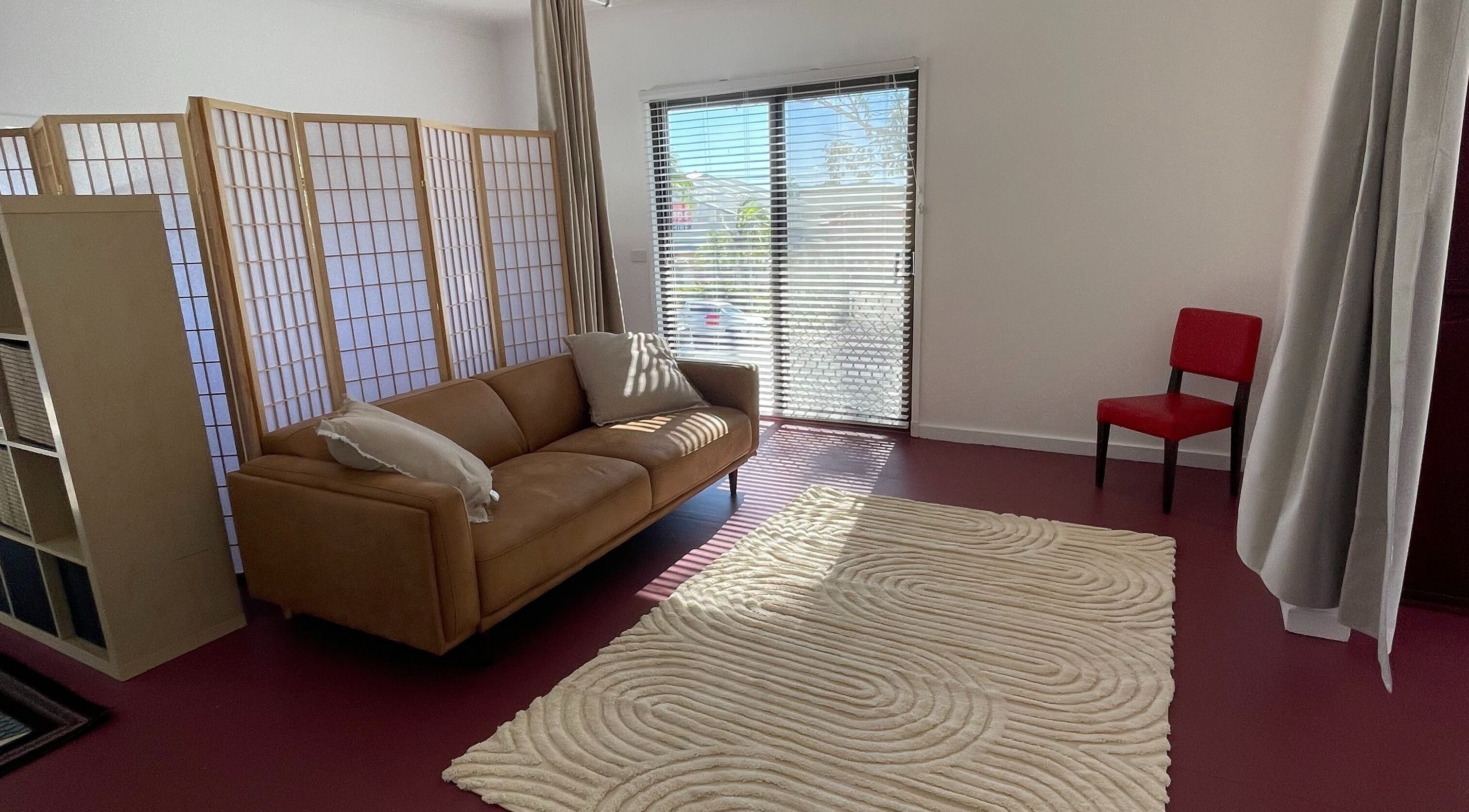 Cozy lounge area at The Biofield Body - Byron Bay, featuring a comfy sofa, red chair, and soft lighting in Byron Bay, New South Wales, AU.