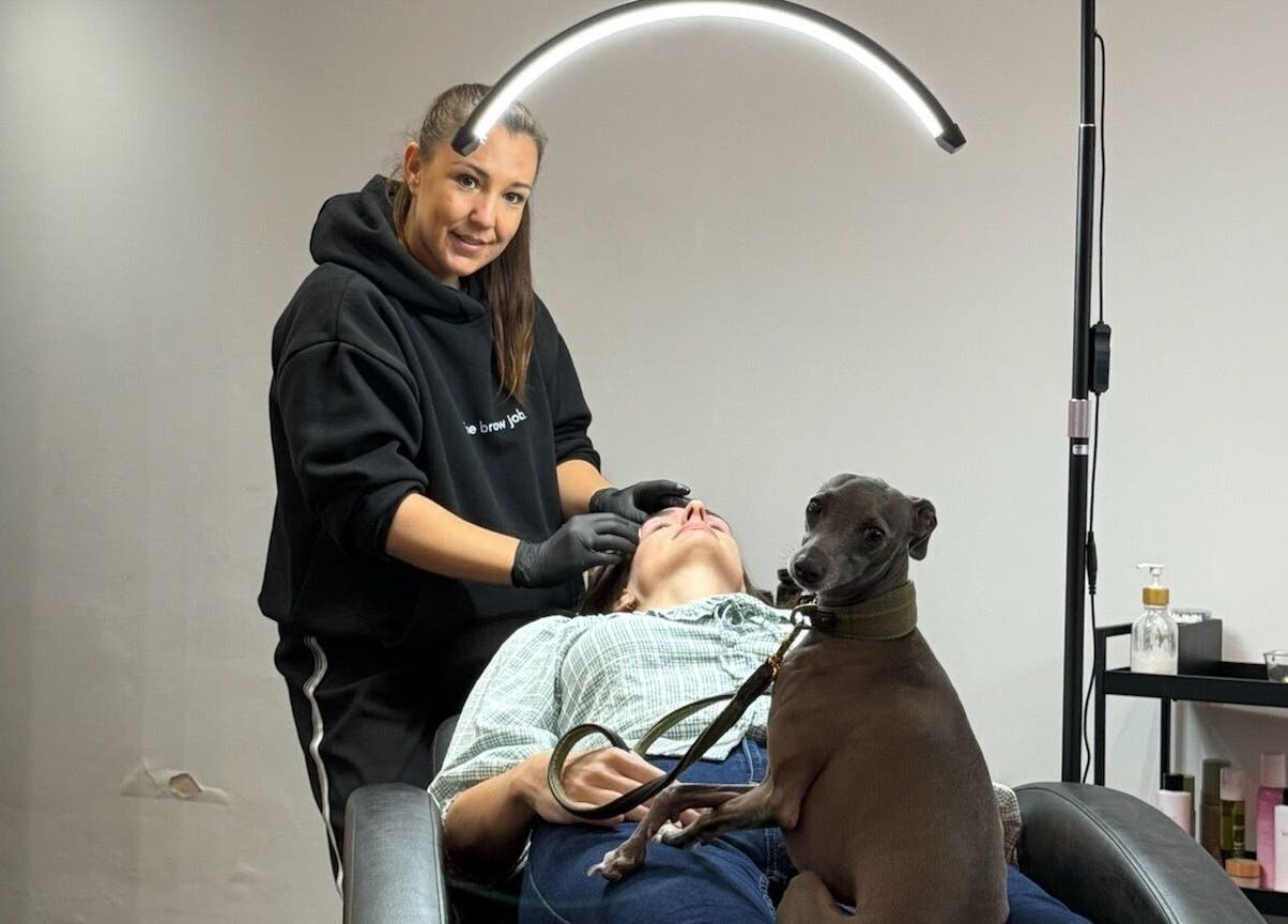 Beauty expert shaping eyebrows at the brow job in Chester, England, GB with a pet dog nearby.