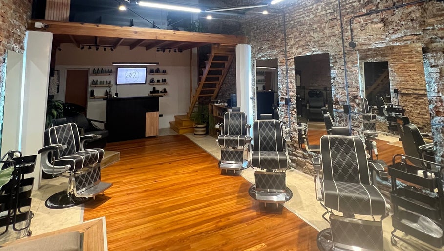 Interior de GM en Gualeguaychú, Entre Ríos, AR: sillas de peluquería modernas y paredes de ladrillo a la vista.