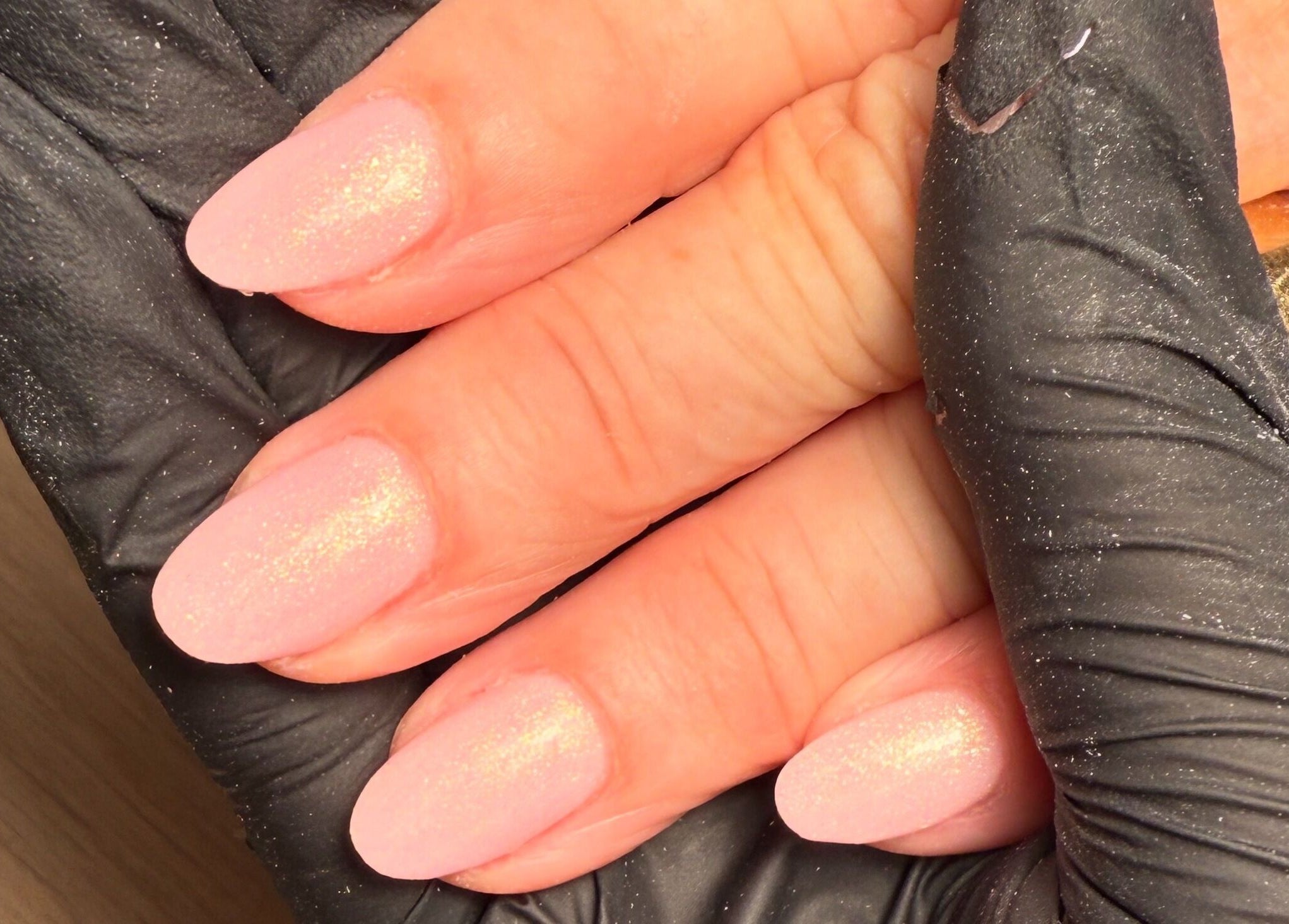 Pink glitter nails at CXM Nails in Bangor, Northern Ireland, GB held by gloved hands.