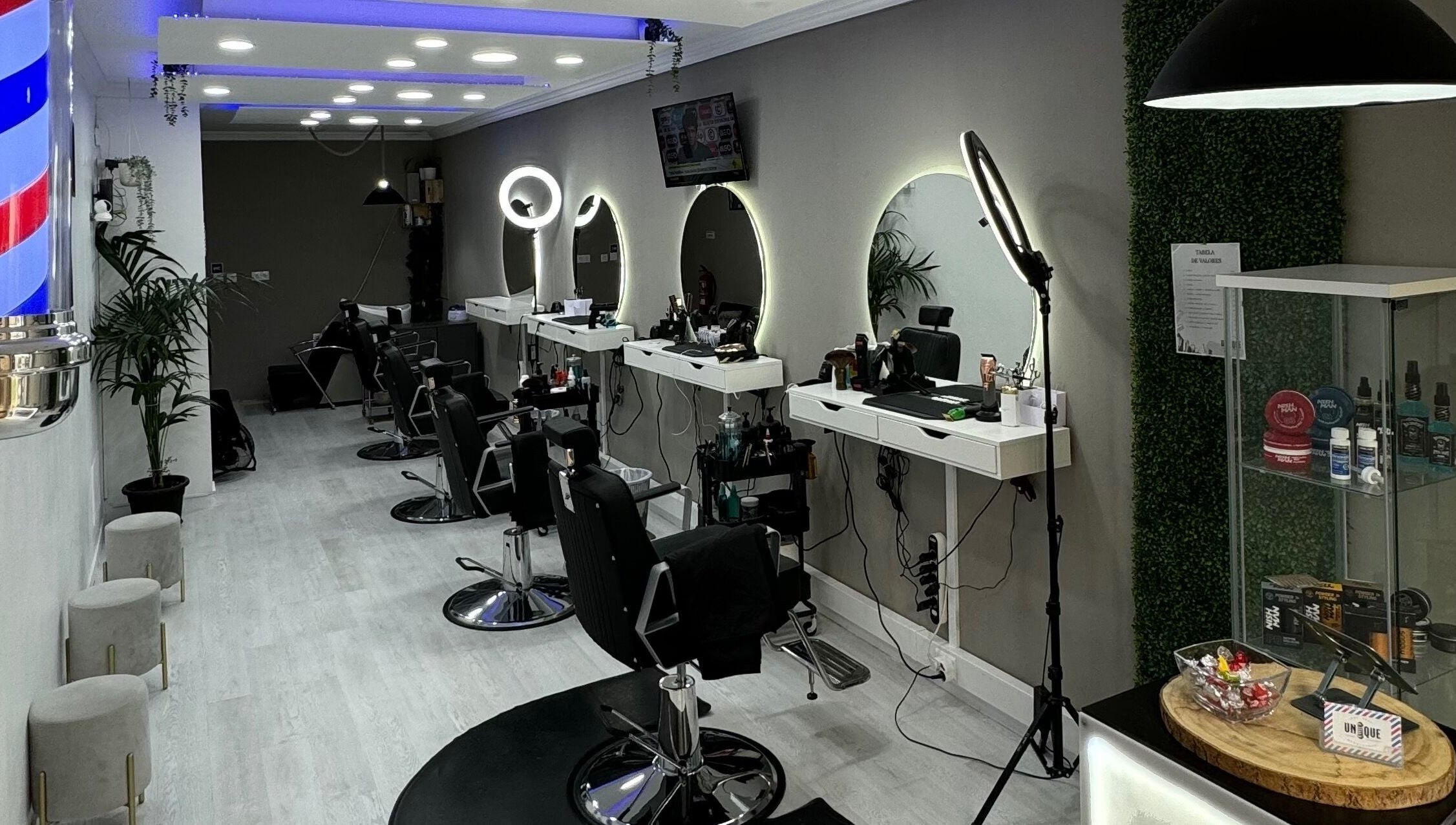 Interior moderno da Unique Barbershop em Estoril, Lisboa, PT, com cadeiras de couro e espelhos iluminados.