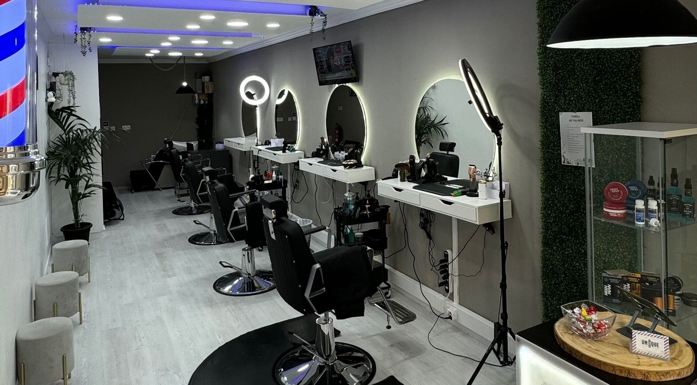 Interior moderno da Unique Barbershop em Estoril, Lisboa, PT, com cadeiras de couro e espelhos iluminados.
