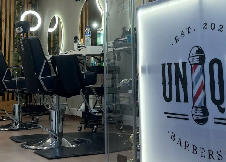 Interior sofisticado da Unique Barbershop em Estoril, Lisboa, PT, com poltronas modernas e espelhos iluminados.