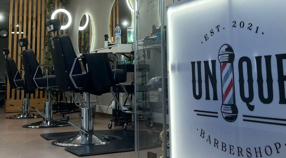 Interior sofisticado da Unique Barbershop em Estoril, Lisboa, PT, com poltronas modernas e espelhos iluminados.
