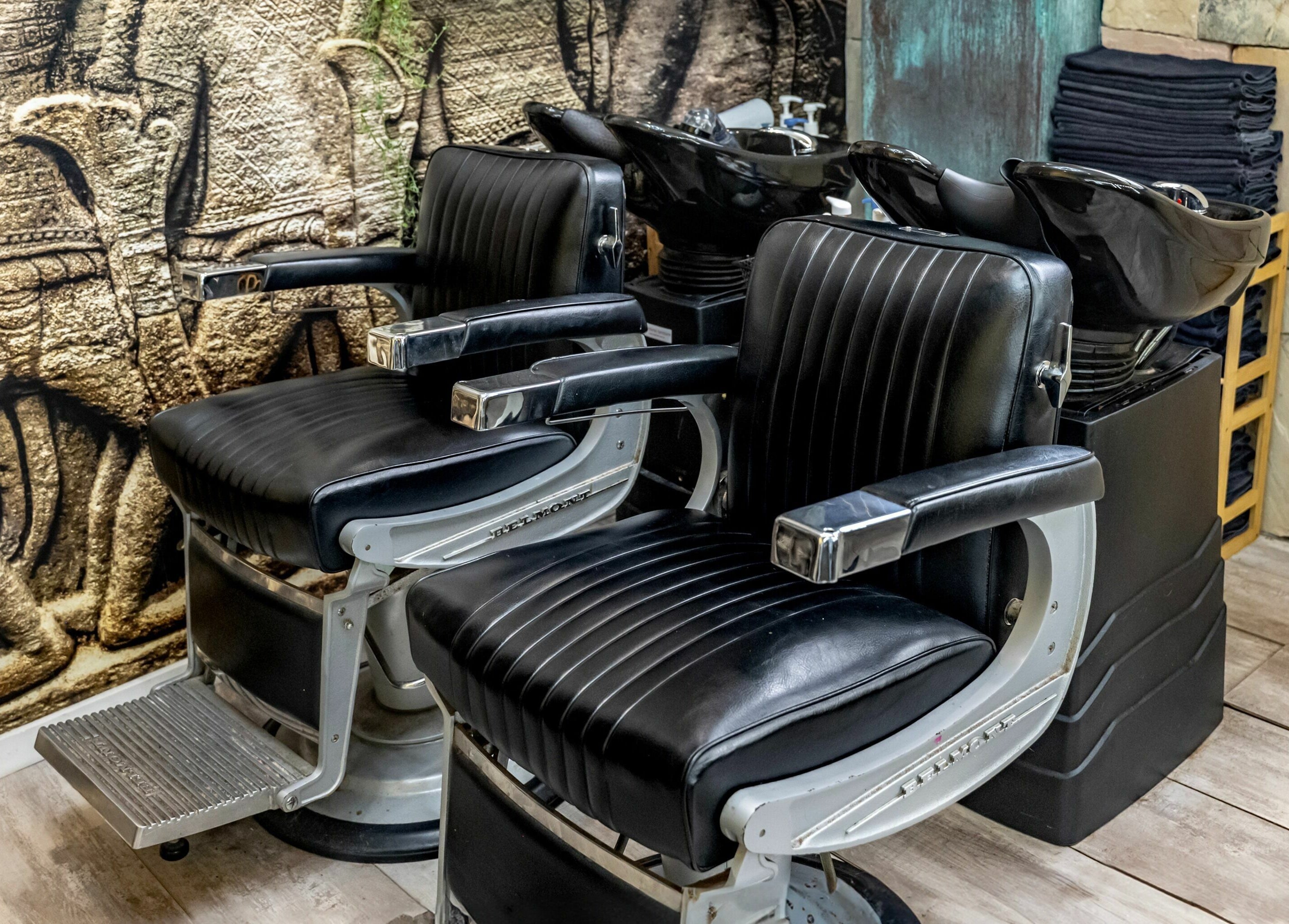 Luxurious black leather barber chairs at Public Hair Studio, Brookvale, NSW, AU against artistic wall backdrop.